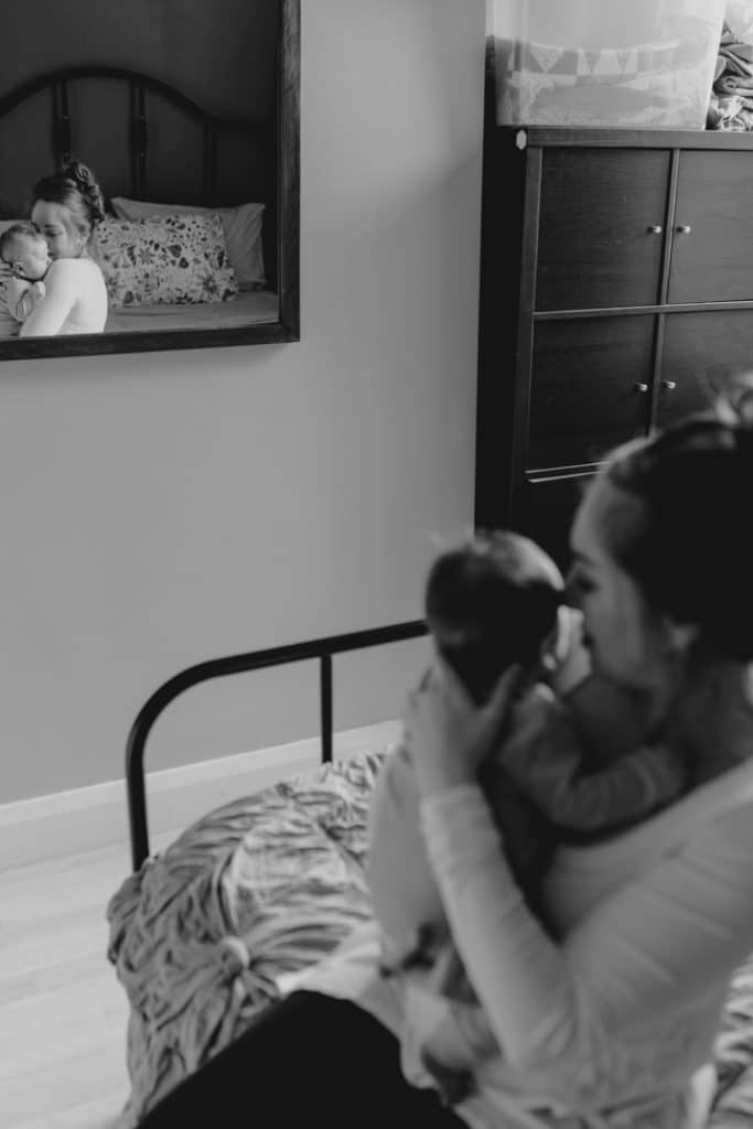 Mum is sitting in the bed and looking at her baby boy. baby boy is looking out at the window.In home photo shoot. Newborn session. Hampshire photographer. Ewa Jones Photography