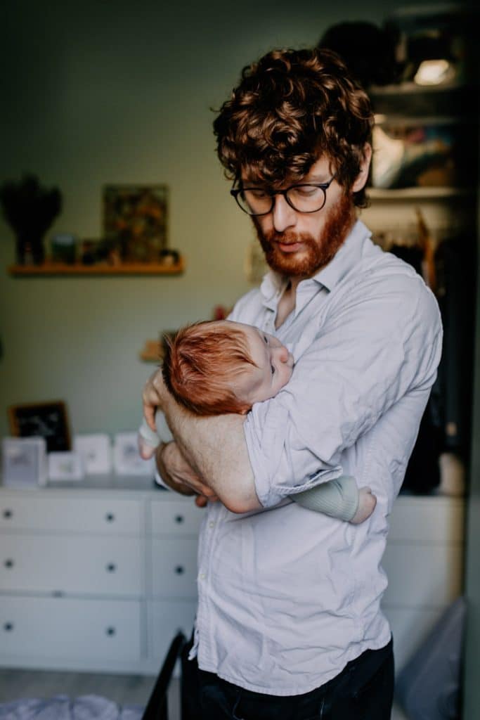 Dad is holding baby boy in his hands. Dad is wearing a light blue shirt and baby boy is looking up. in home newborn photo session. Lifestyle photo shoot at home. Basingstoke newborn photographer. Hampshire newborn photo session. Ewa Jones Photography