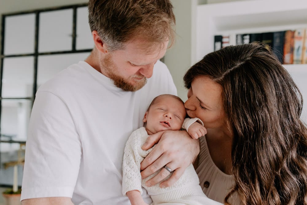 Mum is kissing her newborn baby, dad is holding baby. lovely indoor newborn photo session. Intimate newborn session. Hampshire photographer. Ewa Jones photography