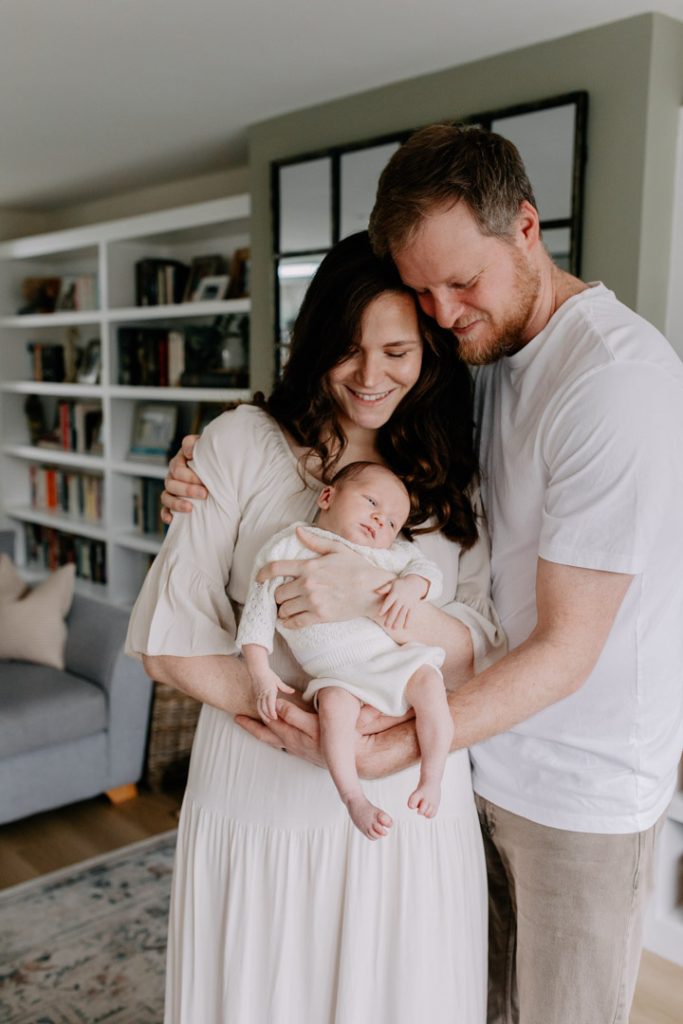 Mum and dad are cuddling and mu, is holding her newborn baby. Newborn photo shoot in the comfort of your own home. Newborn session. Hampshire newborn photographer. Ewa Jones photography