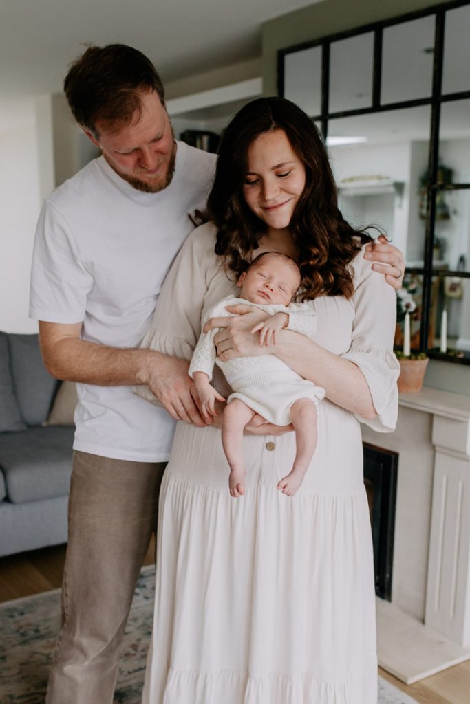Mum and dad are cuddling and mu, is holding her newborn baby. Newborn photo shoot in the comfort of your own home. Newborn session. Hampshire newborn photographer. Ewa Jones photography