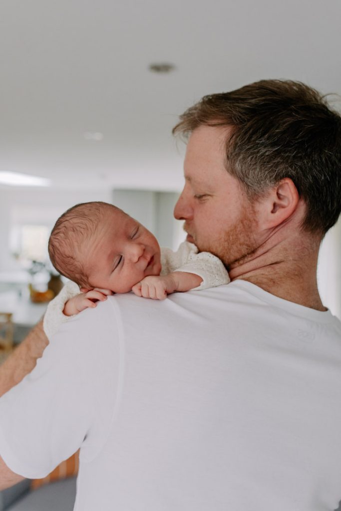 Little newborn baby boy is sleeping over dad's shoulder. Intimate and natural newborn photoshoot in Hampshire. Ewa Jones Photography
