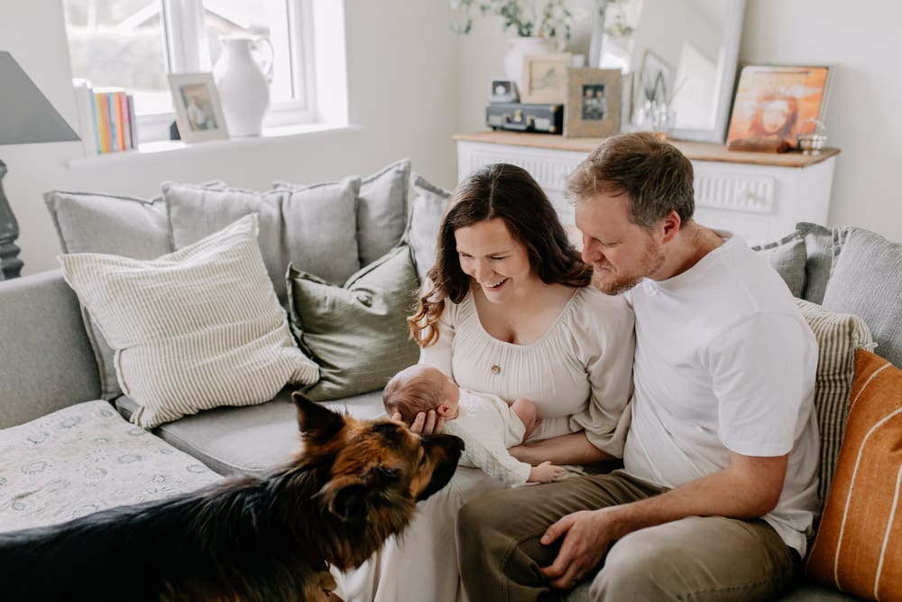 parents are sitting on the sofa and looking at their baby boy. Natural in home newborn photo shoot. Hampshire in home newborn photography. Basingstoke photographer. Ewa Jones Photography