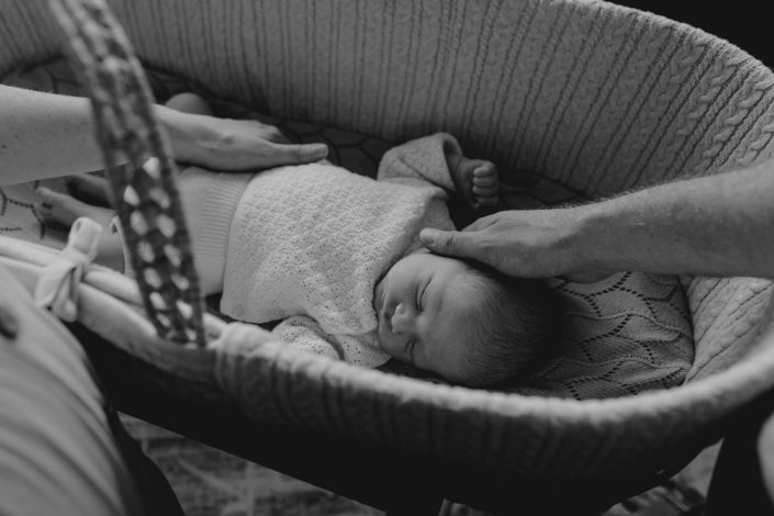 newborn poses. Mum and dad are reaching out to the little baby which is laying in the crib. Ewa Jones Photography