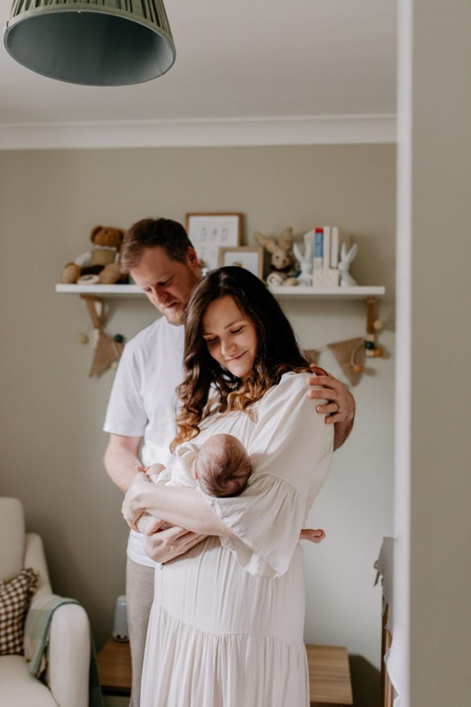 Mum and dad standing in a beautiful natural nursery and looking at their baby boy. Natural photo session. Ewa Jones Photography