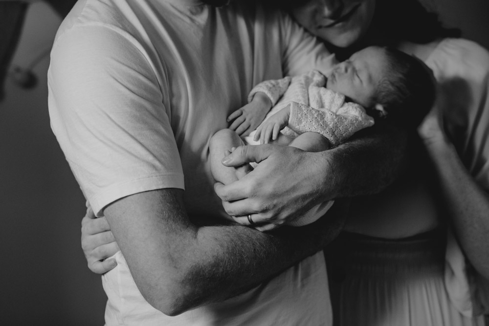 Hampshire newborn photo session. Intimate newborn photo shoot at home. Dad is holding newborn baby and mum is cuddling on the side. Ewa Jones Photography