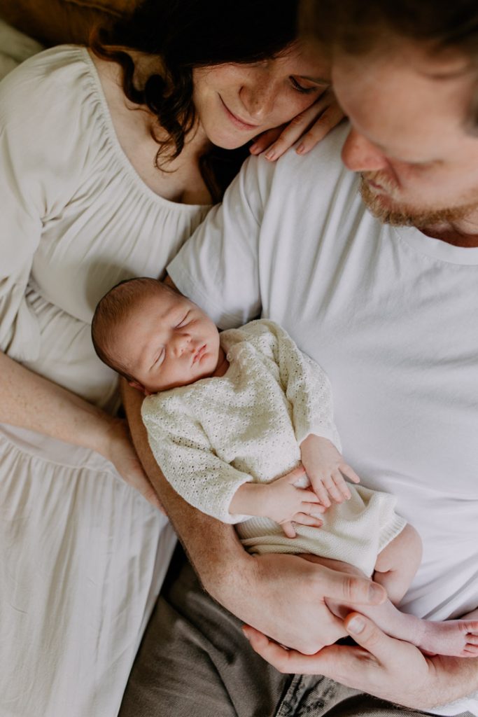 Hampshire newborn photographer. mum and dad are looking down at their baby boy. mum is wearing natural dress and little baby is wearing lovely knitted outfit. Ewa jones Photography