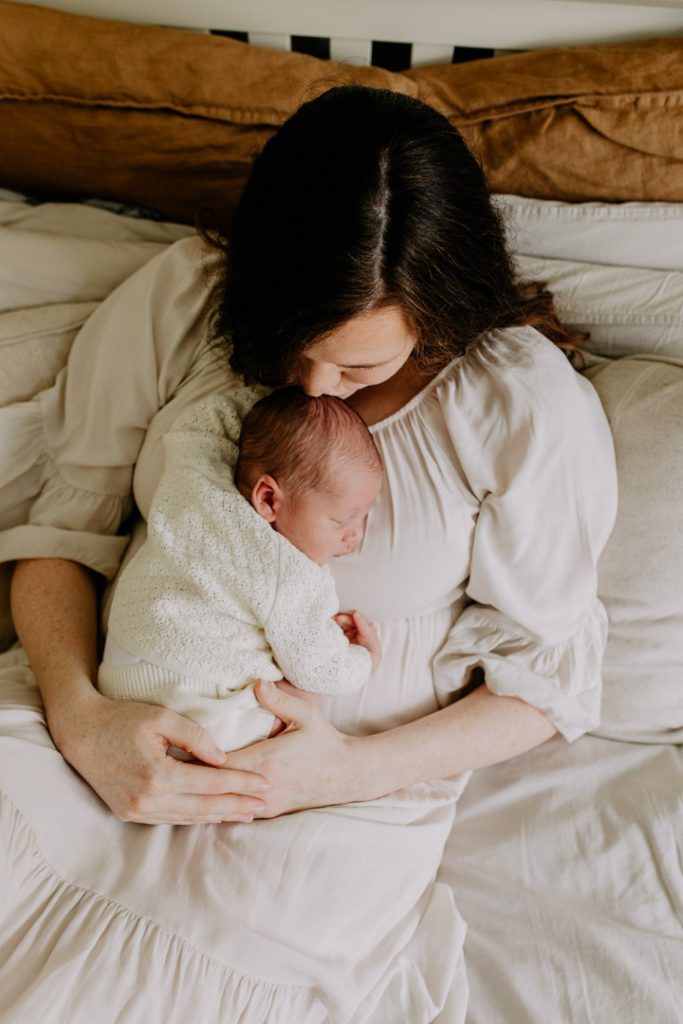 Mum is kissing her baby boy on his head. baby boy is sleeping. Newborn photo shoot at home. Ewa jones Photography, Hampshire photographer