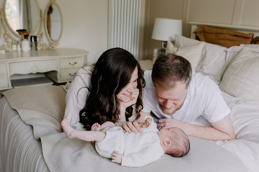 Parents are laying on bed and looking at newborn baby. Ideas for newborn photo shoot. Ewa jones Photography. How to express love during a newborn session