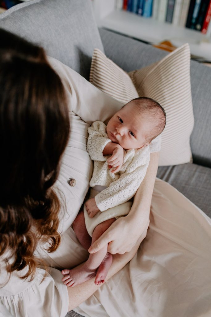Mum is sitting holding her newborn baby and looking at baby. lovely house interior for the newborn photo session. Ewa jones Photography