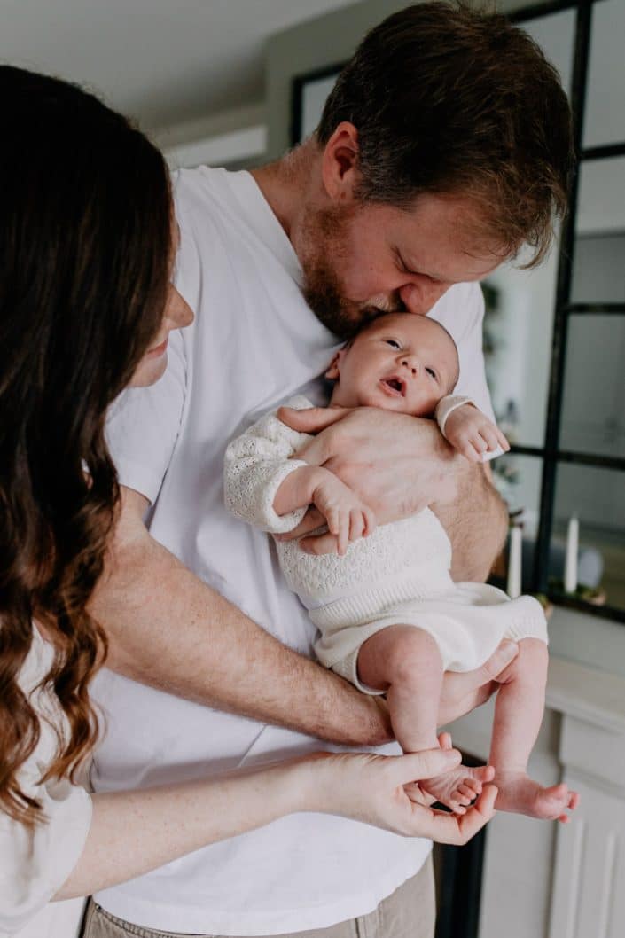 Newborn baby boy is being held by his dad. Mum is next to dad and a baby. Lovely natural photo session in home. Newborn photo shoot in Hampshire. Hampshire newborn photographer. Ewa Jones Photography