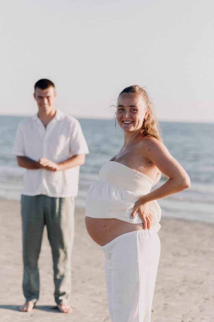 Mum to be is standing in front and her partner is at the back. Lovely happy maternity session at the beach. Hampshire photographer. Ewa Jones Photography