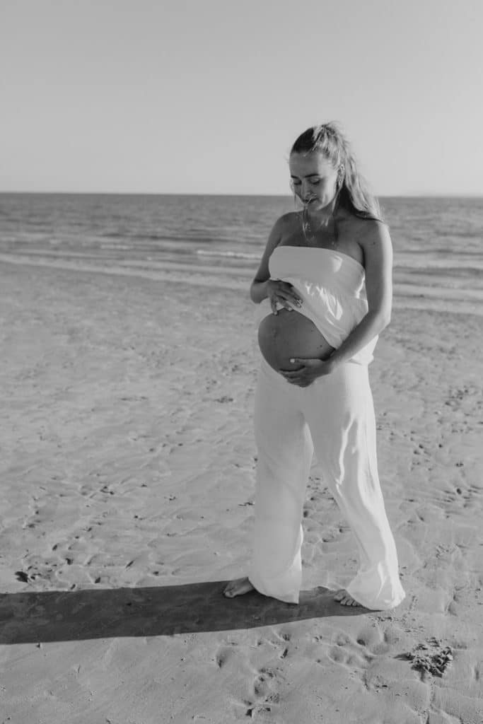 Mum to be is standing at the beach and looking back at her bump. Lovely spring evening. Baby photo shoot at the beach. Hampshire photographer. Ewa Jones Photography