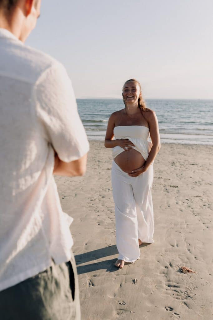 Mum to be is smiling and walking towards her partner. Candid maternity photo shoot at the beach. Maternity photographer in Hampshire. Ewa Jones Photography