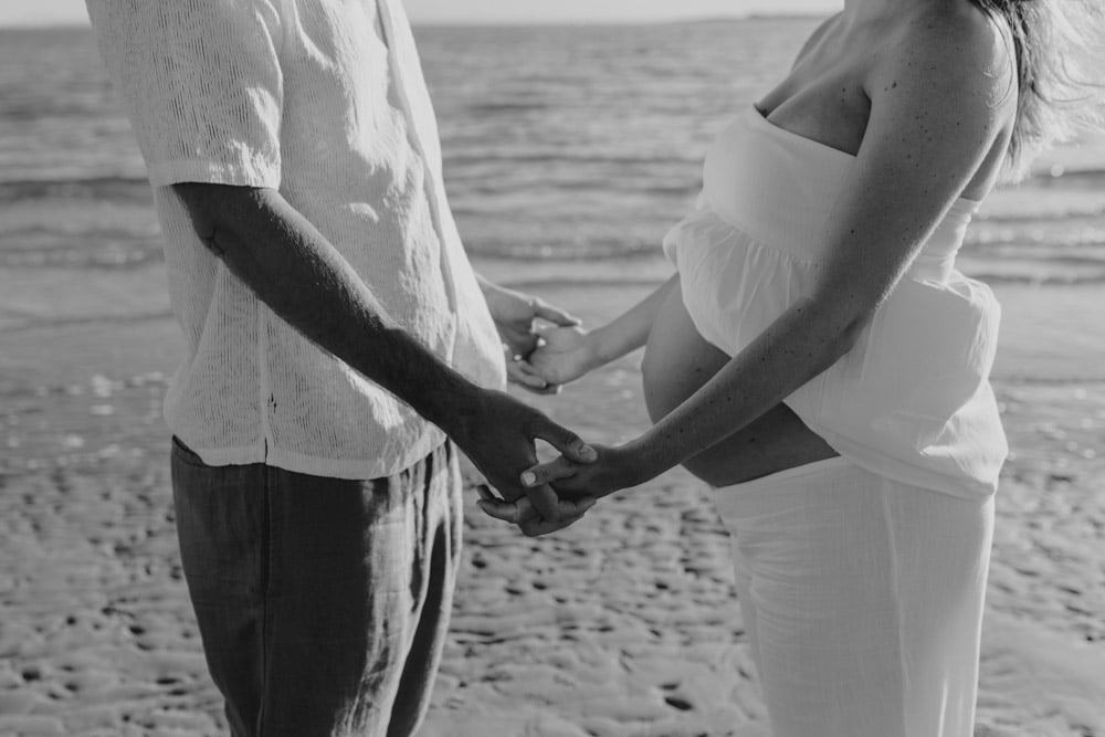 Parents to be are holding hands. Black and white photo. Maternity shoot at the beach. Bump photography. Ewa Jones Photography