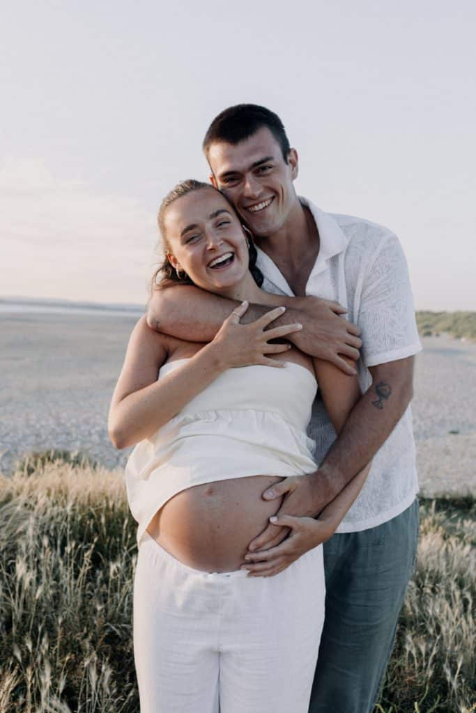 Parents to be are smiling and looking at the camera. Spring photo shoot at the beach. Maternity shoot. Maternity photo session by the sea. Ewa Jones Photography