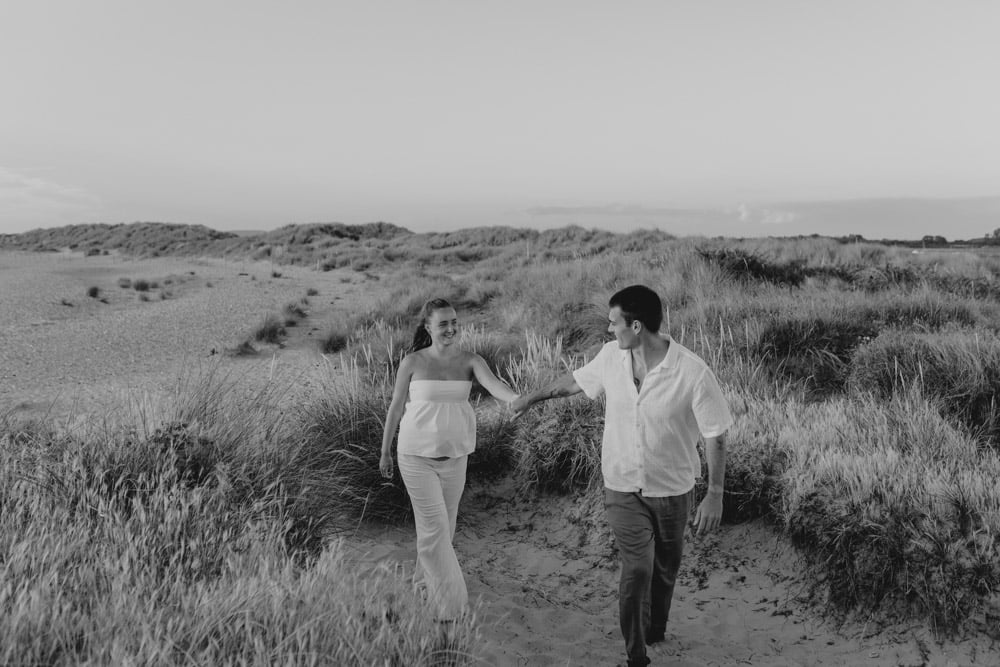 Black and white image of couple to be walking on the beach and smiling. Lovely photo session at the beach. Hampshire photographer. Ewa Jones Photography. maternity photo session by the sea