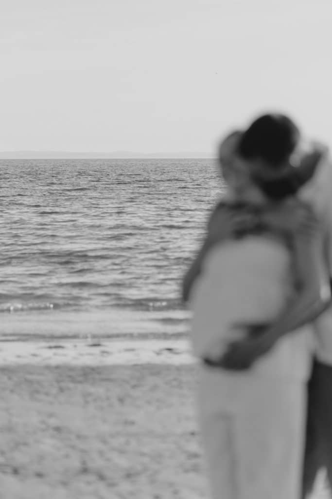black and white off focus image of pregnant mum and her partner. Camera is looking at the sea. Maternity photography in Hampshire. Hampshire photographer. Ewa Jones Photography