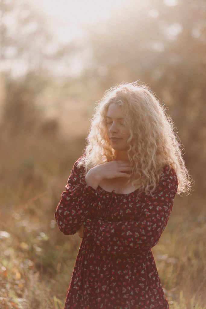 woman is wearing red dress and standing in the field. she has her eyes closed. lovely natural photo session outside. Women photoshoot. hampshire female photographer. Ewa Jones Photography