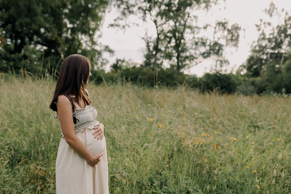mum is standing and looking at the field of flowers. Mum is wearing lovely dress. Maternity shoot outdoors. Natural session. Hampshire and Basingstoke photographer. Ewa Jones Photography