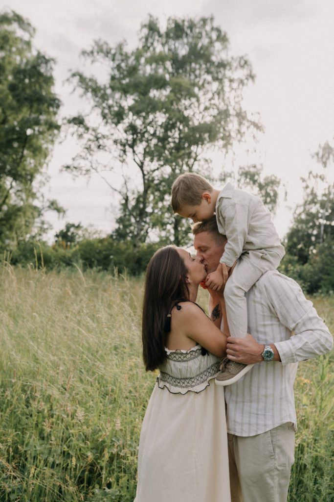 Mum and dad are kissing and dad is holding his boy on his shoulders. Family photo session outdoor. Family session. Hampshire photographer. Ewa Jones Photography. how to prepare for family session