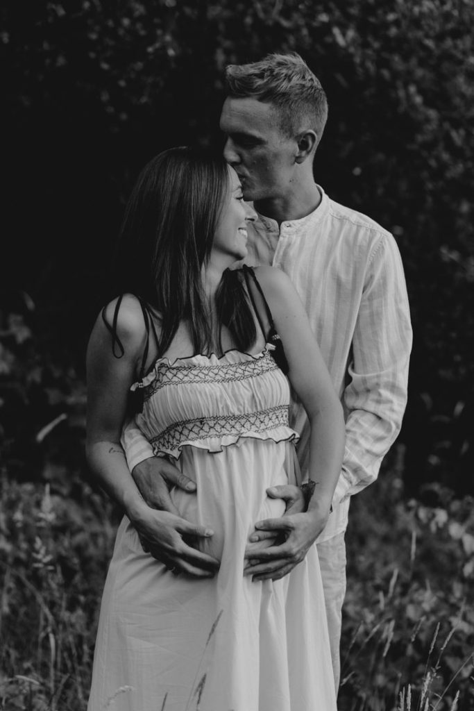 Mum and dad are cuddling and dad is kissing his partner on top of her head. Maternity session. Maternity poses for outside session. Maternity shoot. Ewa Jones Photography