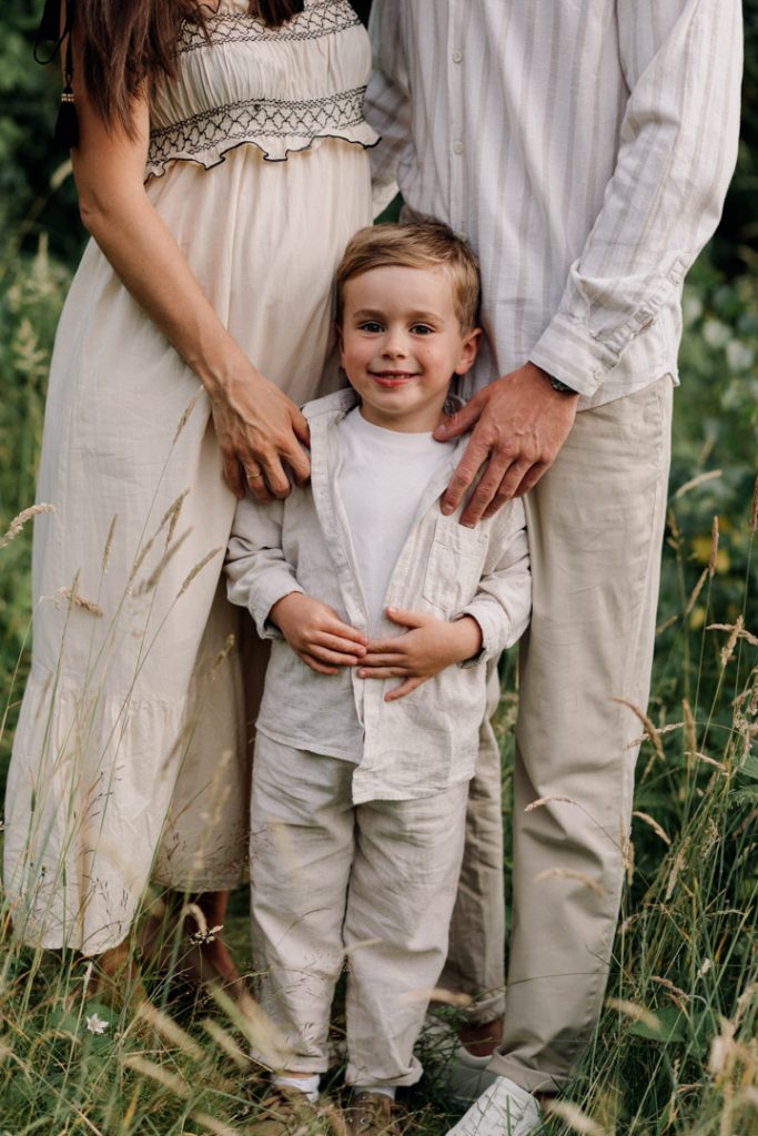 What to wear for a family photo session. Natural family photography. Mum and dad are cuddling close. their son is standing and looking at the camera. How to prepare for a family session. Hampshire photographer. Ewa Jones Photography