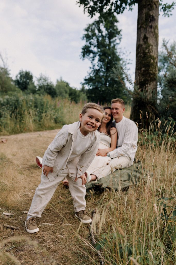 outdoor family shoot. boy is looking at the camera and smiling. Mum and dad are sitting on the blanket and smiling. family photo shoot in Hampshire. Ewa Jones photographer