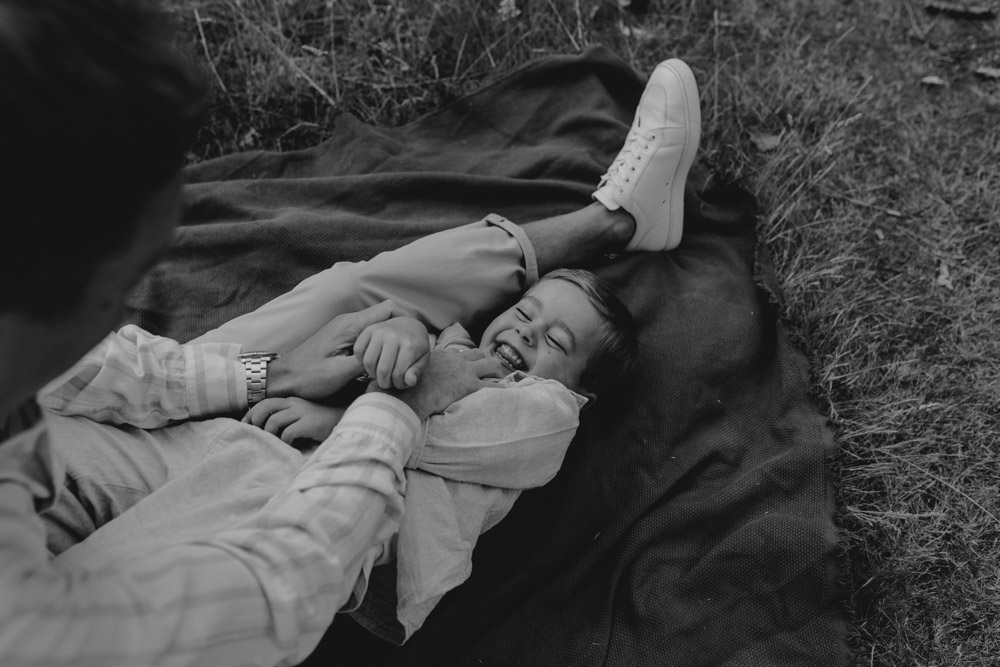 dad is cuddling his boy and the boy is smiling. natural family session. how to prepare for family session. family photo shoot. Hampshire photo shoot outside. Family photographer. London photographer. Ewa Jones photographer