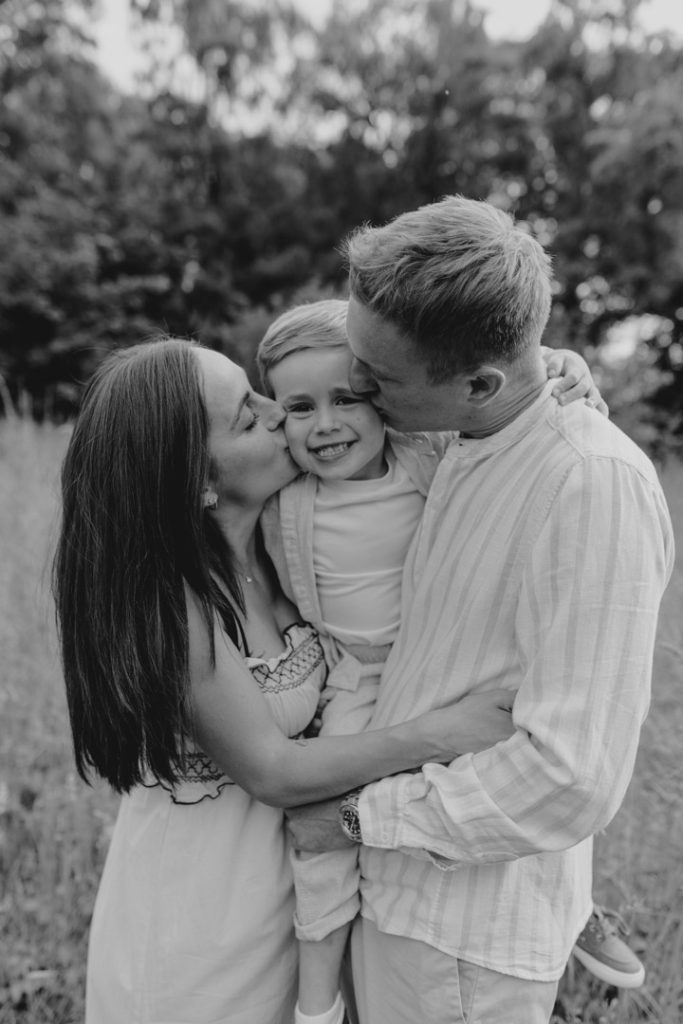 Mum and dad are kissing their boy in his cheeks. Black and white image. Natural family photo session. Hampshire family photography. Hampshire photographer. Ewa Jones Photography