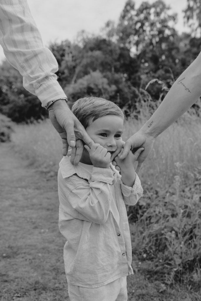 Black and white image of boy holding mums and dads hands towards his cheeks. Lovely family photo shoot. Photo shoot in Hampshire. Family photographer in Hampshire. Hampshire photographer. Ewa Jones Photography