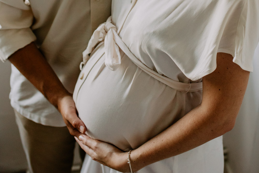 Mum and dad are cuddling and holding baby bump. In home pregnancy session. London photoshoot. Hampshire photographer. Ewa Jones photographer