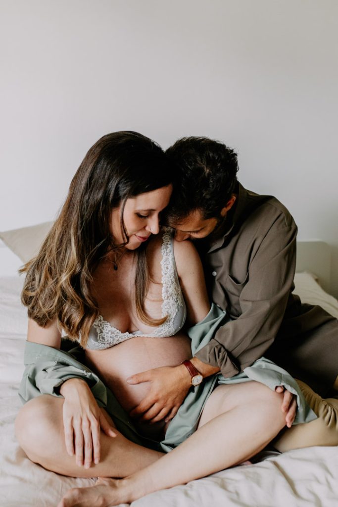 expecting parents are sitting on the bed and cuddling close. Intimate maternity shoot. in home maternity photography. bump photo shoot. Ewa jones photography