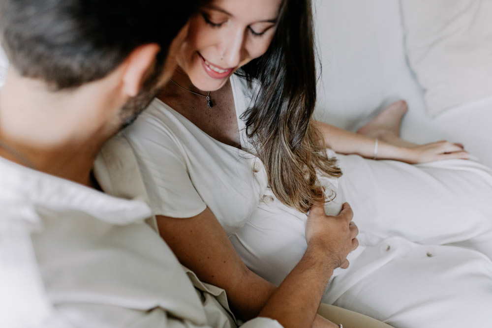 Close up of baby bump. Dad to be is holding baby bump and mum to be is gently smiling. Maternity photo session at home. Photography tips on how to create stunning maternity photos