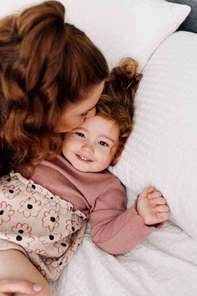 Mum is kissing her little girl on her forehead. Lovely natural moment between mum and daughter. Family photographer in Hampshire. Ewa Jones Photography
