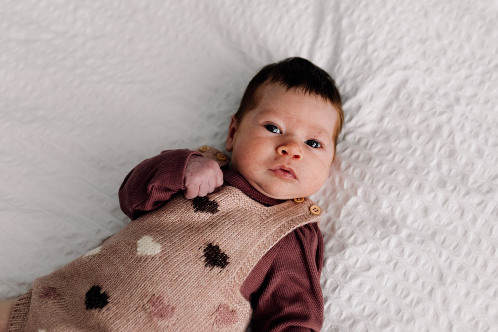 Newborn baby girl is wearing lovely autumn outfit. Laying on the bed and looking at the camera. Hampshire newborn photographer. Ewa Jones Photography