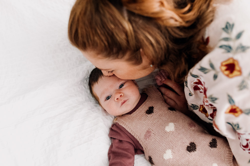 Mum is kissing baby girl on her forehead. In-home newborn photoshoot. Hampshire photographer. Ewa Jones Photography