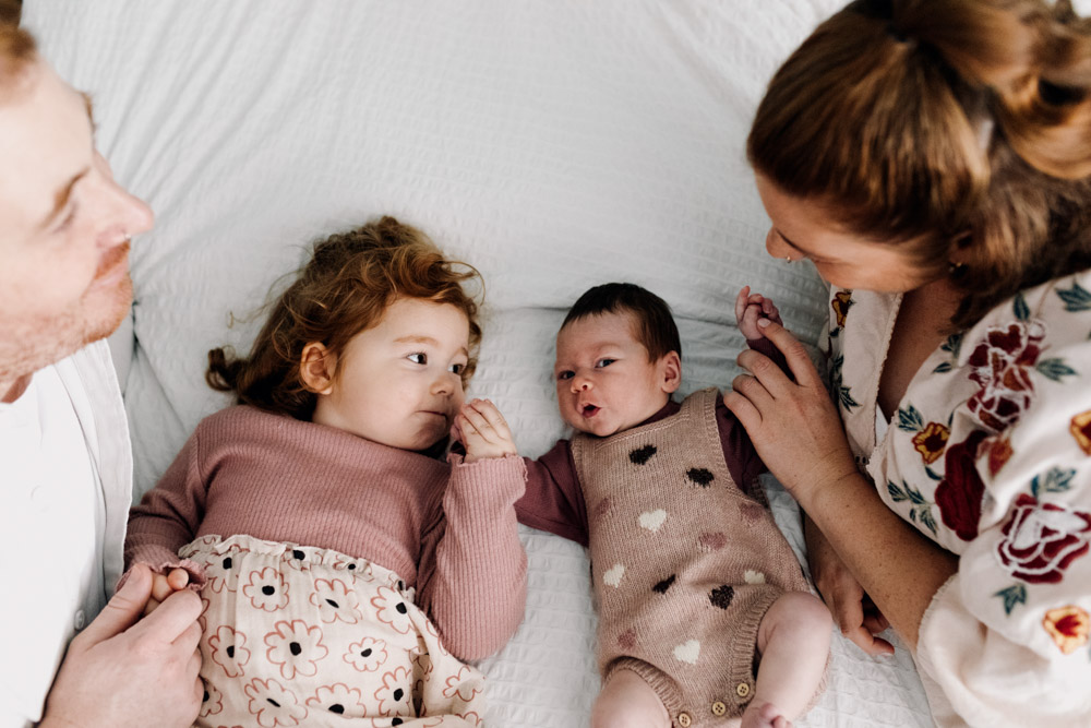 baby girl and toddler are laying on the bed. mum and dad are on the side of them. Natural family photo session. in home newborn photoshoot. Hampshire newborn photographer. Ewa Jones Photography