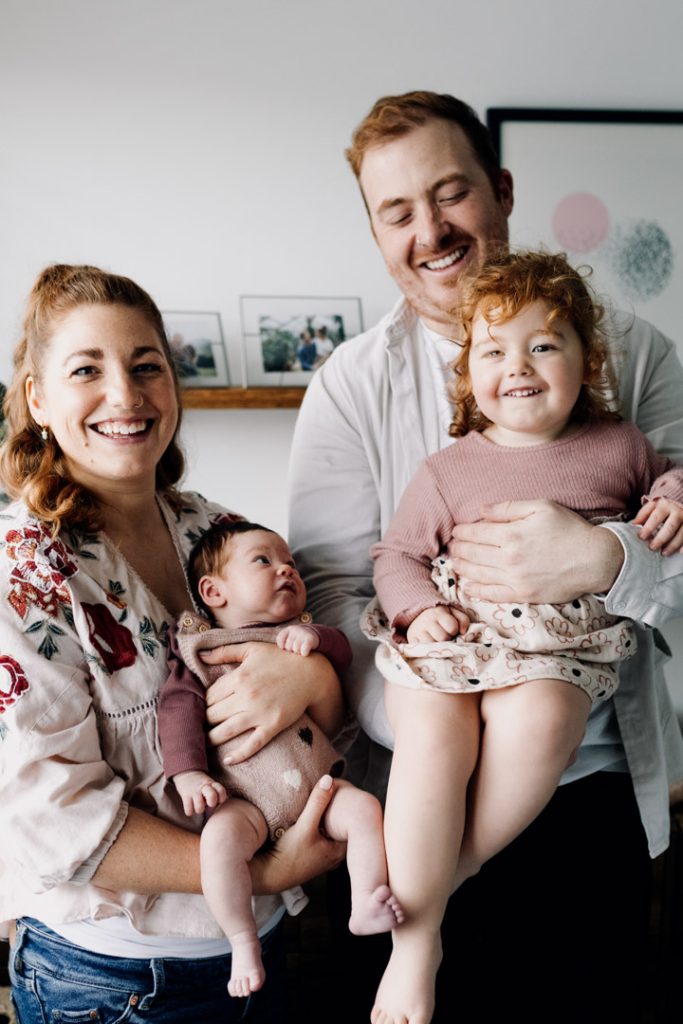 Family of four is standing and smiling to the camera. newborn photo session at home. Hampshire photographer. Ewa Jones Photography