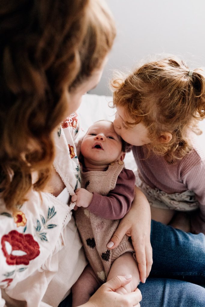 Toddler sister is kissing newborn baby sister. Lovely in home natural newborn photo session. Hampshire photographer. Ewa Jones Photography