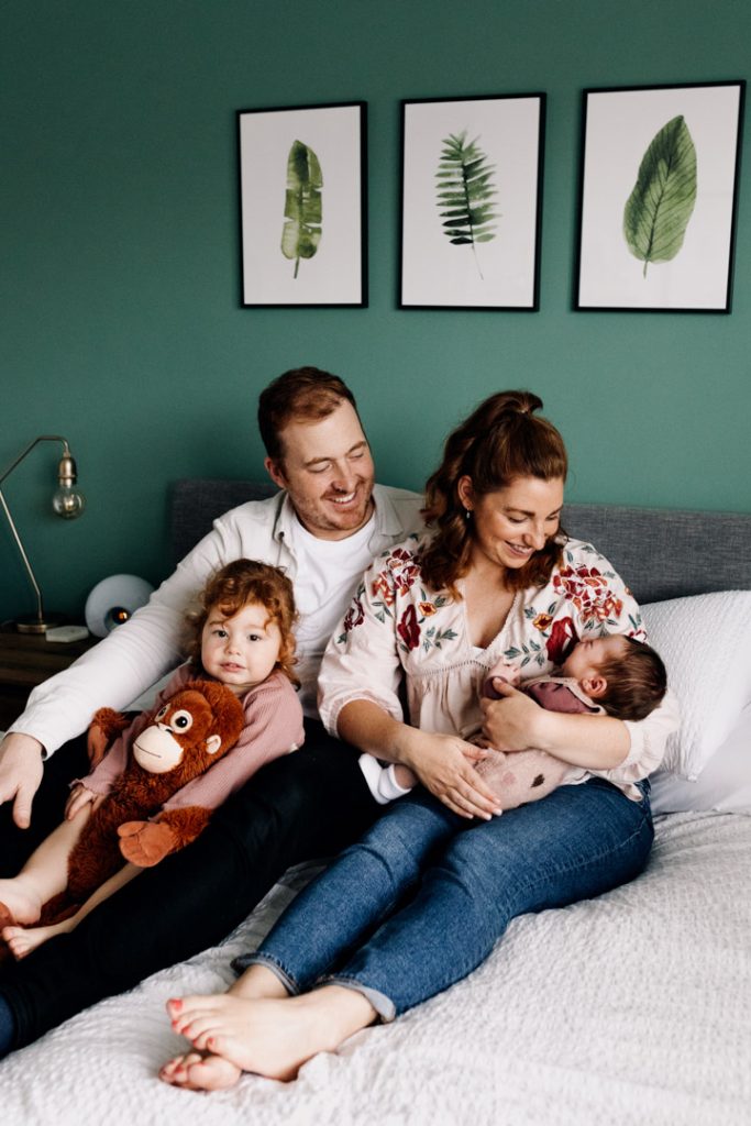 Family is sitting on the bed and cuddling.in home newborn photo shoot in Hampshire. Mum is looking at baby girl. Ewa Jones Photography