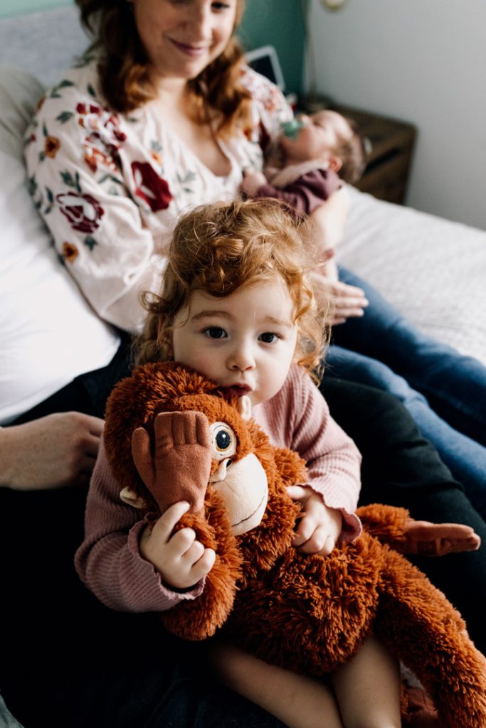 Toddler girl is holding monkey and doing peek a boo. lovely interactive newborn photo session at home. Hampshire newborn photographer. Ewa Jones Photography