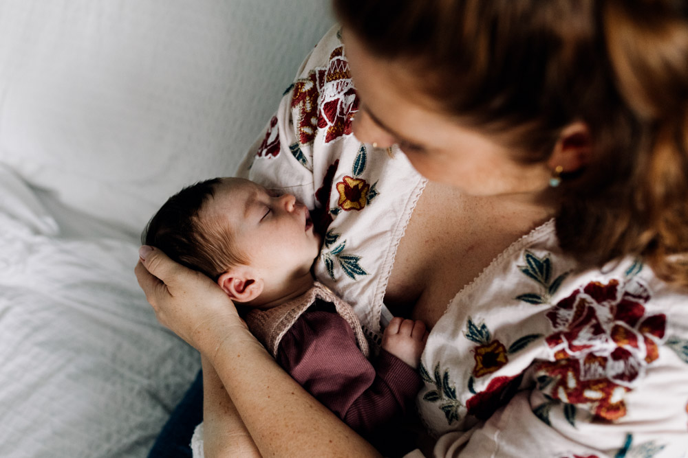 Mum is holding newborn baby in her arms and looking down on baby. Hampshire and Basingstoke newborn photoshoot. Ewa Jones Photography. In-Home Newborn Photo Sessions With a Toddler: Relaxed, Real and Full of Joy