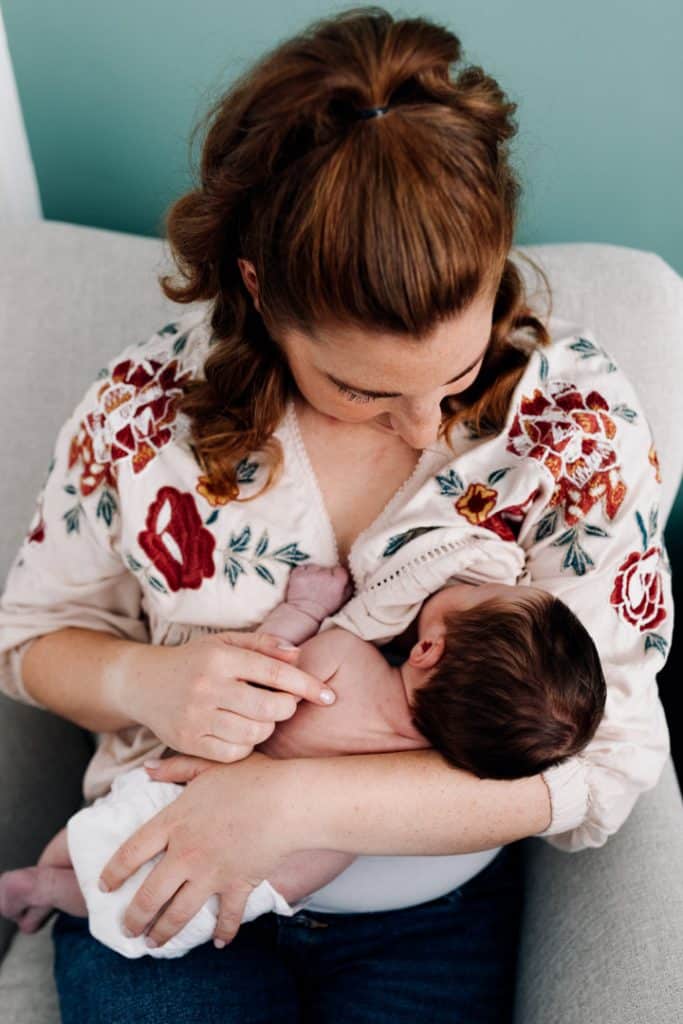 Mum is feeding her newborn baby girl. Hampshire photographer. natural in-home newborn photo session. Mum is looking down on the baby. newborn photo shoot in Hampshire. Ewa Jones Photography