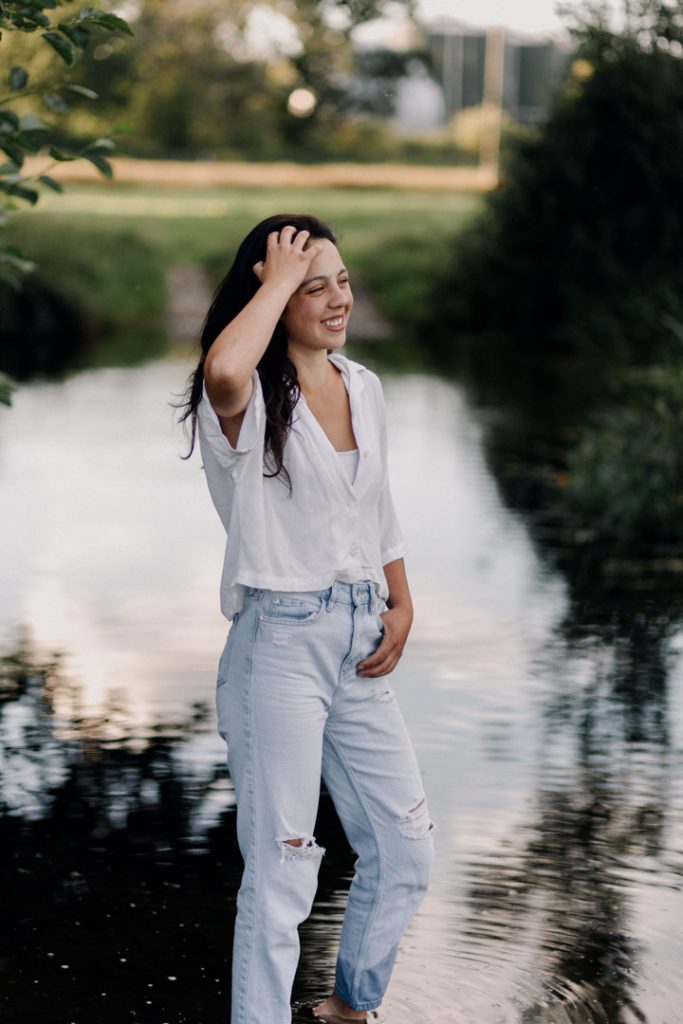 female is standing in the shallow water and touching her hair. She is smiling. She is wearing nice white top and jeans. Lovely natural moment. Capturing the important moments of your life. Hampshire photographer. Hampshire photo session. Ewa Jones Photography