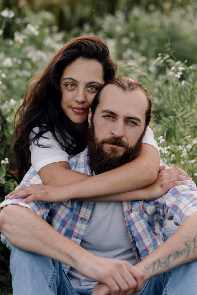 Lovely image of couple looking at the camera. Man is sitting on the ground and his partner is cuddling him from behind. Hampshire photo session. Hampshire and Basingstoke photographer. Ewa Jones Photography