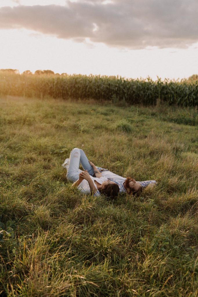 Couple is laying on the grass and holding hands. Couple's photo session during golden hour. Hampshire photo session. Hampshire couple's photographer. Ewa Jones Photography