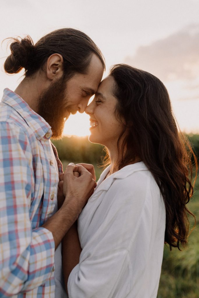 Couple holding hands and touching foreheads at sunset during a relaxed outdoor photoshoot in Hampshire, smiling and sharing an intimate moment in natural light. Hampshire couple photographer. Ewa Jones Photography