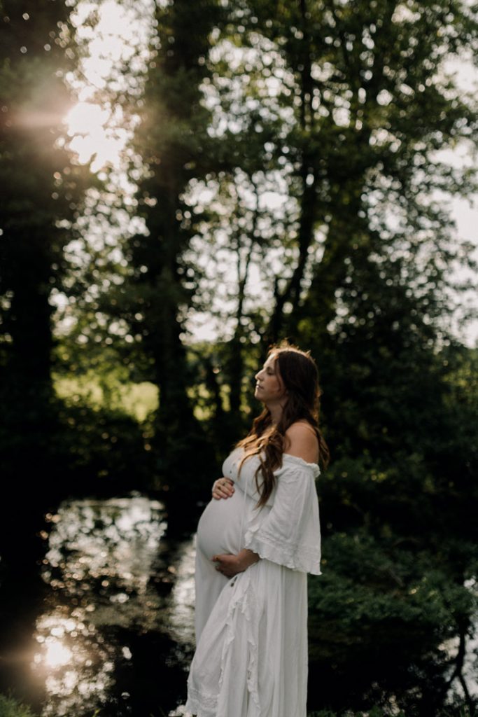 mum is cuddling her baby bump and has her eyes closed. natural and calm maternity photo session. moment in time. Pausing and enjoying the beauty of pregnancy. Lovely golden hour is creating stillness and gentle atmosphere. Hampshire baby bump photo shoot. Ewa Jones Photographer