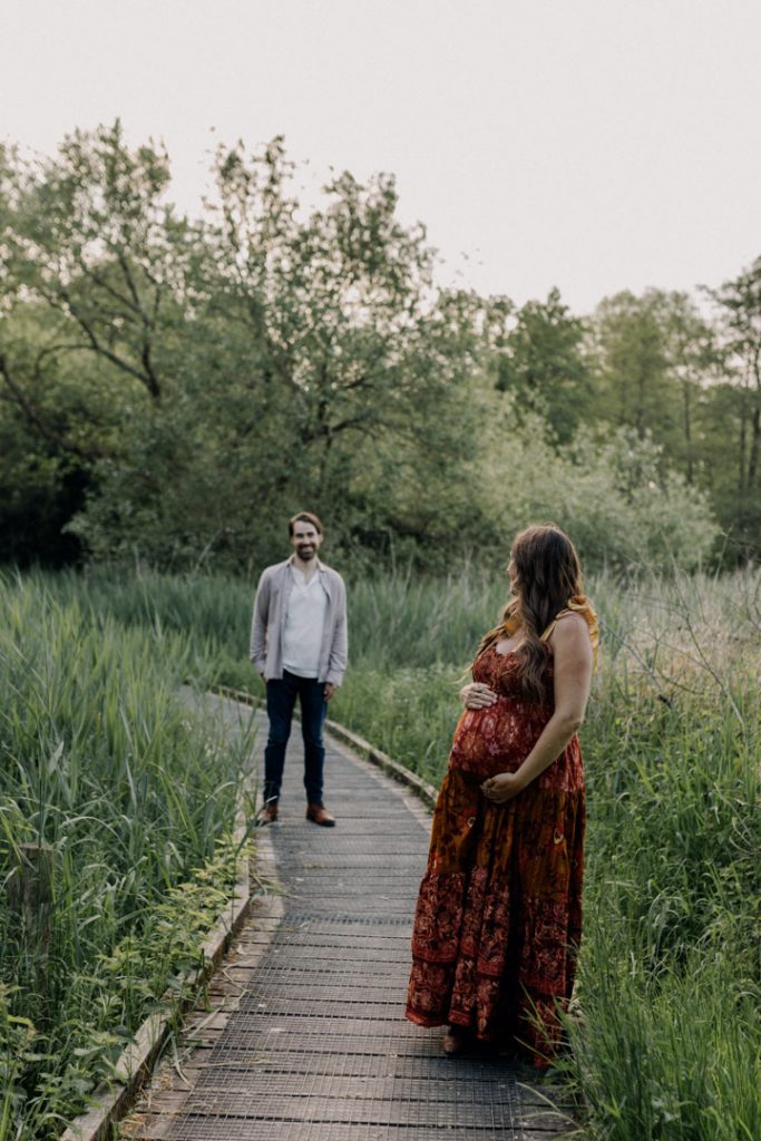 mum and dad are standing and mum is looking back at his husband. nice and fun bump photo session. Outdoor and golden hour maternity shoot. Basingstoke photographer. Ewa Jones Photographer